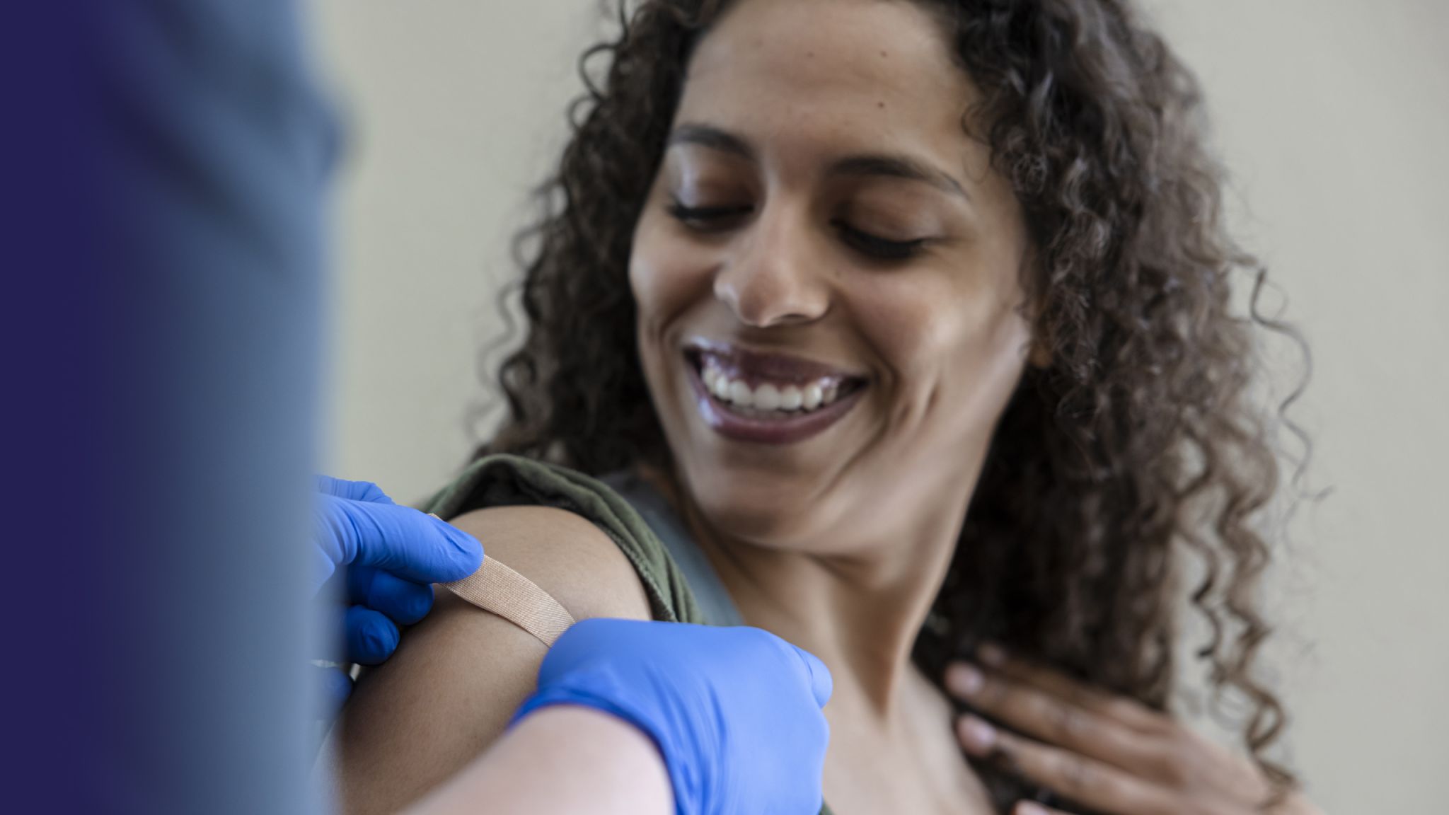 Close up of healthcare professional placing a band aid/plaster on a smiling female patients arm.